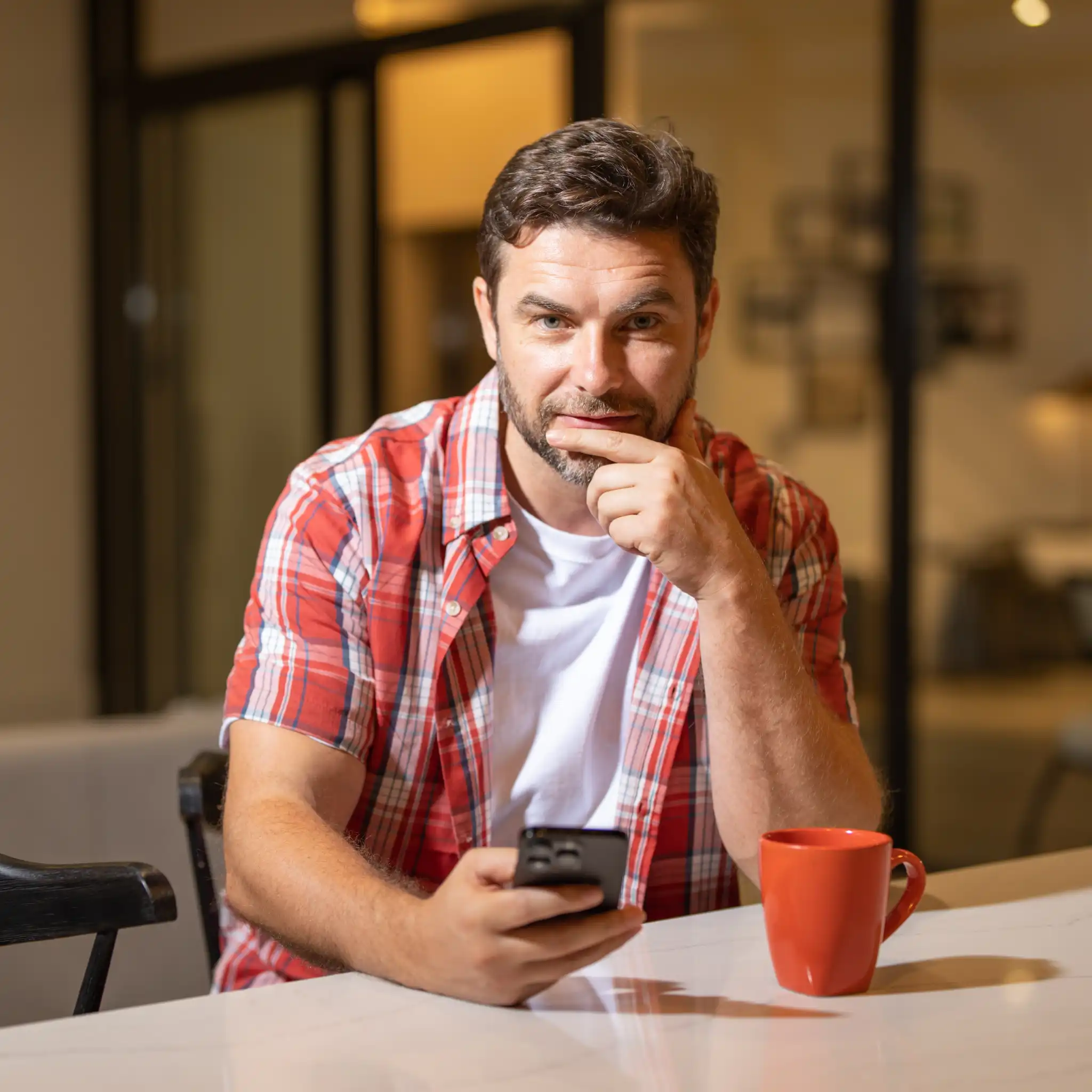 james-belly-blog-avatar A man in a red plaid shirt sitting at a table with a red coffee mug, holding a phone and thoughtfully looking at the camera. James Belly blog avatar